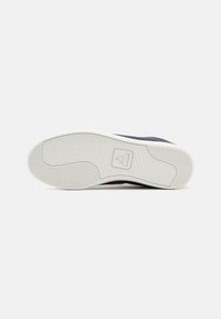 Black sneaker with a textured rubber sole, featuring a white midsole, herringbone pattern, and a logo imprint on the sole.