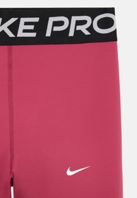 Leggings de sport roses avec une taille noire portant "NIKE PRO" en texte blanc et un logo Nike blanc sur la jambe. Texture de tissu lisse.