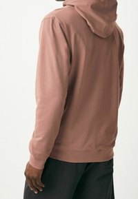 Felpa con cappuccio di colore rosa polveroso, caratterizzata da maniche lunghe e una vestibilità rilassata. Materiale di cotone liscio con un design semplice e senza motivi visibili.