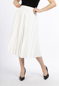 Witte plissé midi-rok met een gladde tailleband, vloeiende stof en zachte textuur, gecombineerd met zwarte puntige pumps.