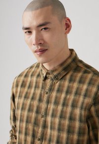 Braun-grün kariertes Button-Up-Shirt aus strukturiertem Stoff, mit Kragen und sichtbaren Knöpfen auf der Vorderseite.