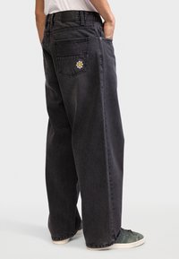 Jean en denim noir ample avec un patch floral sur la poche arrière, cinq poches et une coupe droite. Tissu texturé.