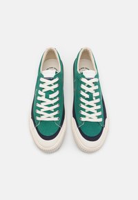 Zelené plátěné tenisky s bílými tkaničkami, kontrastními námořnickými akcenty, gumovými podrážkami a zaobleným špičatým designem. Na jazyku se nachází logo značky.
