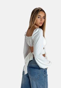 Hvid langærmet bluse med puffærmer og en bindebag-funktion, parret med høj talje blå denim jeans. Glat tekstur, afslappet design.