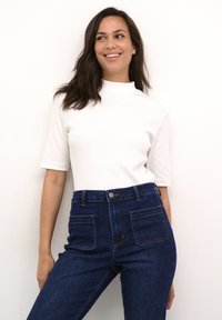 Maiou alb cu mâneci scurte și model ridat, cu un guler înalt, combinat cu blugi din denim albastru închis, cu talie înaltă, prevăzuți cu buzunare în față și în spate.