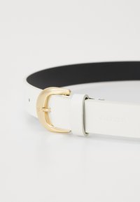 Cintura in pelle bianca con interno nero, dotata di fibbia in metallo dorato. Accenti notevoli includono un logo Calvin Klein impresso sul cinturino.