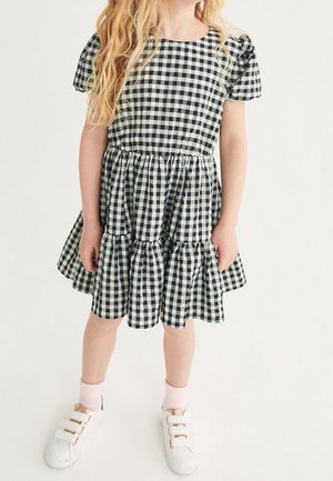 Robe vichy noire et blanche avec manches courtes bouffantes, taille froncée et jupe à volants superposés. Associée à des baskets blanches et des chaussettes roses.