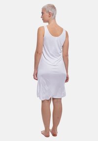Abito bianco senza maniche realizzato in tessuto morbido, con scollatura rotonda e una vestibilità drappeggiata che arriva a metà coscia.