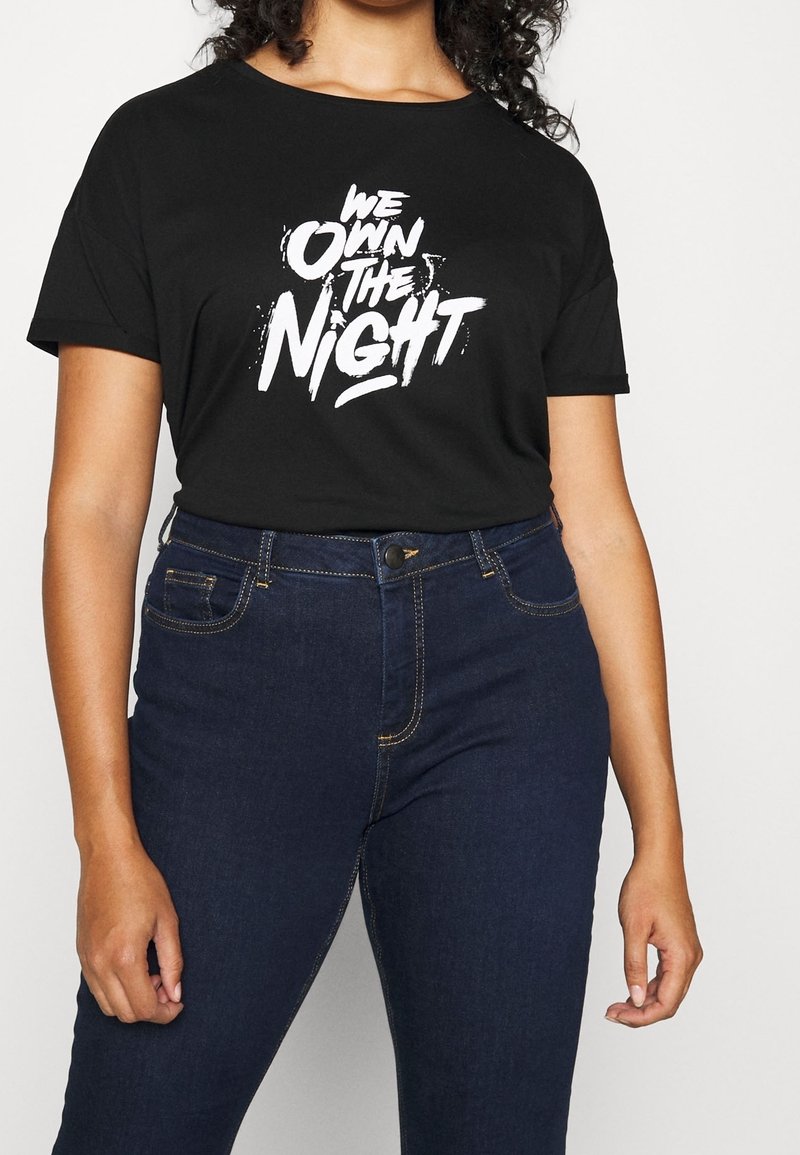 Black cotton t-shirt featuring white graphic text "WE OWN THE NIGHT." Paired with dark blue jeans, displaying stitching details and pockets.