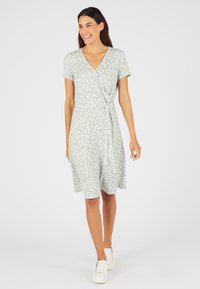 Vestido envolvente floral en verde claro, de manga corta, hasta la rodilla, con un detalle de lazo en la cintura. Combinado con zapatillas blancas.