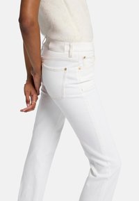 Białe dżinsy w slim fit, z subtelnymi przeszyciami i złotymi akcentami. Posiadają tradycyjny pięciokieszeniowy krój.