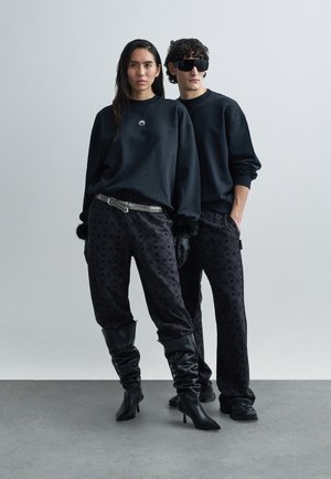 Czarne, oversize'owe bluzy z logo, zestawione z czarnymi spodniami w wzory. Dodatki to srebrny pasek i czarne kozaki za kolano.