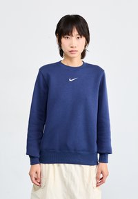 Μπλε ναυτικού φούτερ από μαλακό ύφασμα, με στρογγυλή λαιμόκοψη, μακριά μανίκια και μικρό λευκό λογότυπο Nike στο στήθος.