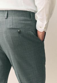 Grå teksturerede bukser med slim fit, der har en baglomme med en knap. Båret med en hvid skjorte med knappede manchetter.