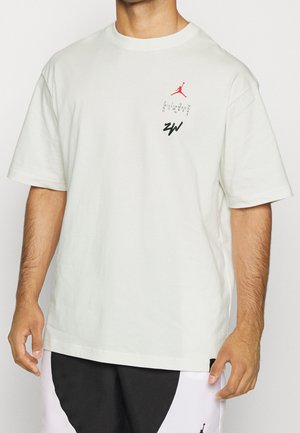 Mężczyzna w białej koszulce Jordan z czerwonym logo Jumpman, napisem „Zion Williamson Number One” oraz czarnymi inicjałami „ZW” na piersi.