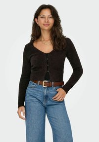 Brown knitted cardigan with a V-neck, long sleeves, and black buttons. Paired with high-waisted blue jeans and a brown belt.