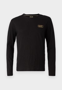 Černé tričko s dlouhým rukávem vyrobené z měkké látky, má malé zlaté logo na hrudi a kulatý výstřih s pohodlným střihem.