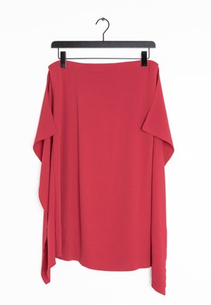 Jupe rouge asymétrique suspendue sur un cintre à pinces noir sur fond blanc.