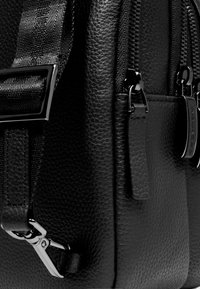 Schwarzer Rucksack aus strukturiertem Leder mit mehreren Reißverschlüssen, schickem Design und silberfarbener Hardware sowie verstellbarem Riemendetail.