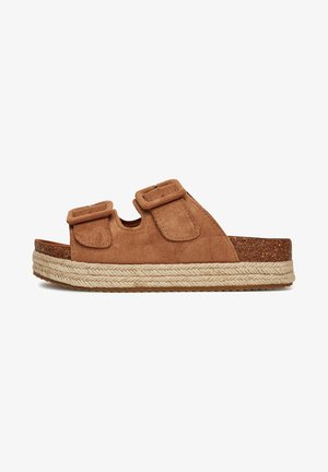 Brown suede slide sandal with two adjustable straps, cork midsole, and braided jute detailing along the edge. Flat, textured rubber sole.