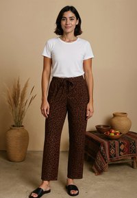 Bruine broek met luipaardprint, met een relaxte pasvorm en een trekkoord in de taille, gecombineerd met een aansluitend wit t-shirt en zwarte slidesandalen.