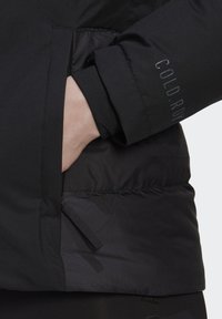 Black padded jacket with a sleek design, featuring a hand in a pocket and sleeve with “COLD.RDY” branding. Smooth, matte texture.