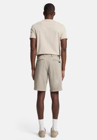 Beige t-shirt, grijze shorts met een rechte snit, zakken met ritsen en lichtgekleurde schoenen. Het achteraanzicht toont schone lijnen en een eenvoudig ontwerp.