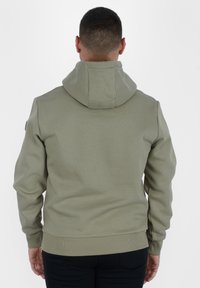 Felpa verde oliva chiaro con un grande cappuccio, polsini e orlo a coste. Realizzata in tessuto liscio, presenta una sottile texture senza motivi visibili.