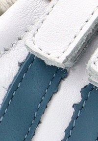 Zapato de cuero azul y blanco con correas de velcro. Presenta franjas de colores horizontales, una textura suave y costuras visibles a lo largo de los bordes.