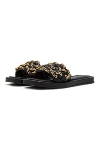 Sandales plates noires avec des brides en cuir tressé entrelacées de chaînes dorées, présentées côte à côte sur un fond blanc.