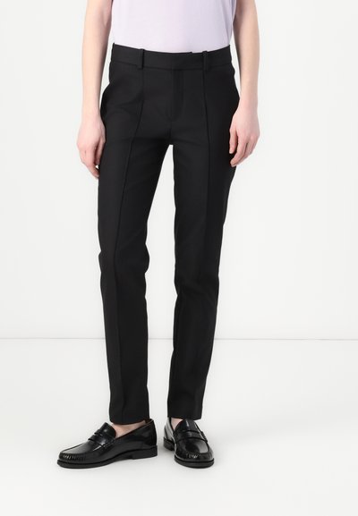 Pantalons noirs ajustés avec une coupe plate et des plis, présentant une texture lisse et une coupe slim, associés à des mocassins noirs brillants.
