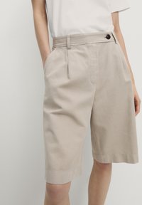 Beige bomuldsshorts med lige snit, synlige sidelommer og en enkelt knaplukning i taljen, med foldet kantdetalje.