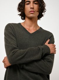 V-Ausschnitt Pullover in dunkelorange, aus weichem, strukturiertem Stoff. Lange Ärmel und lockere Passform, die Arme vor der Brust verschränkt.