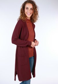 Burgundy open-front cardigan with textured fabric, two front pockets, long sleeves, and ribbed edges, layered over a striped turtleneck.