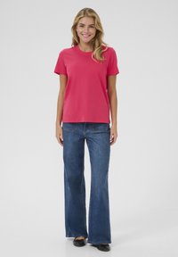 T-shirt en coton rose à manches courtes, associé à un jean en denim bleu foncé à pattes d'éléphant et des chaussures plates noires. Design simple et coupe décontractée.