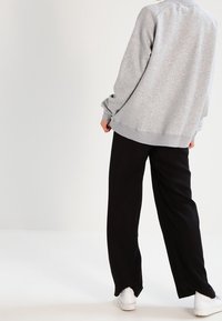 Sudadera gris clara con un corte relajado, escote redondeado y puños acanalados, combinada con pantalones de pierna ancha negros y zapatillas blancas.