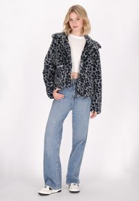 Giacca in pelliccia finta grigio maculato leopardata con colletto, due tasche e chiusura a bottoni, abbinata a jeans a gamba larga azzurri e sneakers.