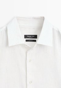 Chemise blanche à manches longues avec fines rayures verticales grises, col classiquement ouvert, et étiquette noire visible portant l'inscription "Massimo Dutti, Made in Egypt".