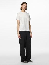 T-shirt blanc à manches courtes avec un col rond, associé à un pantalon noir ample et des chaussures noires à bout pointu avec un motif texturé.