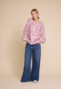 Bluse med blomstermønster i lys rosa og blå, med vide ermer og nøkkelhull-udskæring, parret med brede denimbukser.