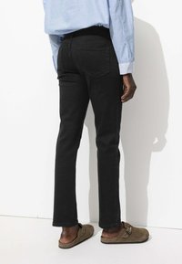 Jeans en denim noir à coupe slim, avec deux poches arrière et une finition lisse. Associés à une chemise à rayures bleu clair et des mocassins marron.