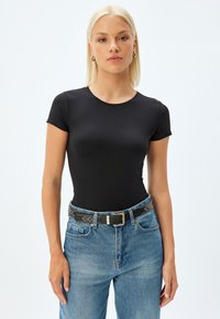 Sort kortærmet T-shirt med rund hals, lavet af strækbart stof; båret med blå denimjeans og et sort med nitter bælte.