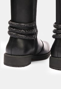 Botas de tobillo de cuero negro con tres bandas decorativas de textura y un cierre lateral, con suela de goma y tacón plano.