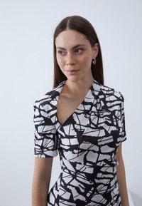 Rochie cu model alb-negru, având un design unic off-shoulder, mâneci scurte și o siluetă ajustată, cu forme și texturi abstracte.