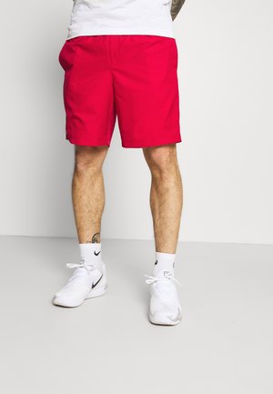 Rote Badeshorts mit elastischem Bund, knielang; kombiniert mit weißen Sportschuhen und weißen Socken mit schwarzen Akzenten.