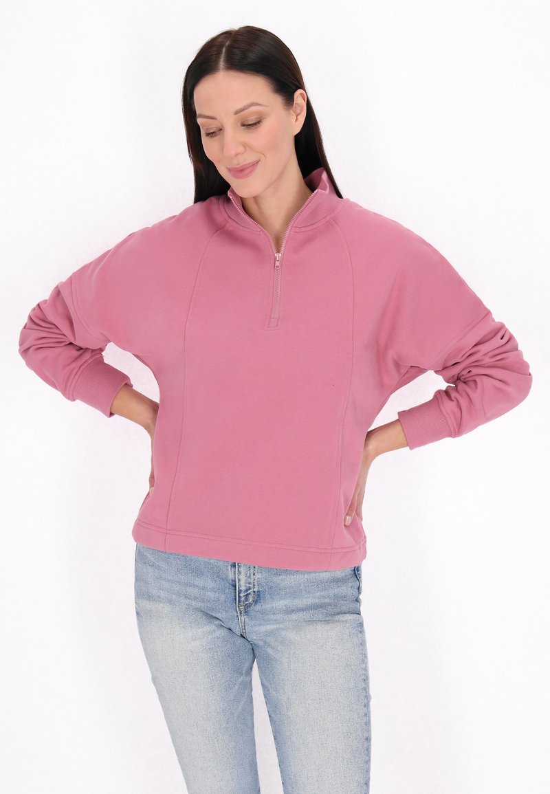 Lichtroze zip-up sweatshirt met een relaxed fit, lange mouwen en geribbelde boorden, gecombineerd met lichtblauwe jeans voor een casual look.