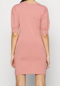 Różowa bawełniana sukienka o dopasowanym kroju, z bufkami na krótkich rękawach i dekoltem w łódkę. Gładka faktura, długość do kolan, bez widocznych wzorów ani zdobień.