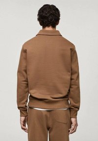Brauner, strukturierter Pullover mit Kragen, gerippten Bündchen und Saum. Getragen mit passender Hose, die eine Tasche auf der Rückseite hat.