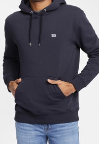 Mörkblå huvtröja i bomullsblandning, med en framficka, dragsko i huvan och en liten broderad "Lee"-logga på bröstet.