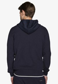 Navy hættetrøje med ribbet tekstur, der har et kontrasterende lysere bånd ved kanten og en glat hætte. Ingen synlige logoer eller detaljer.